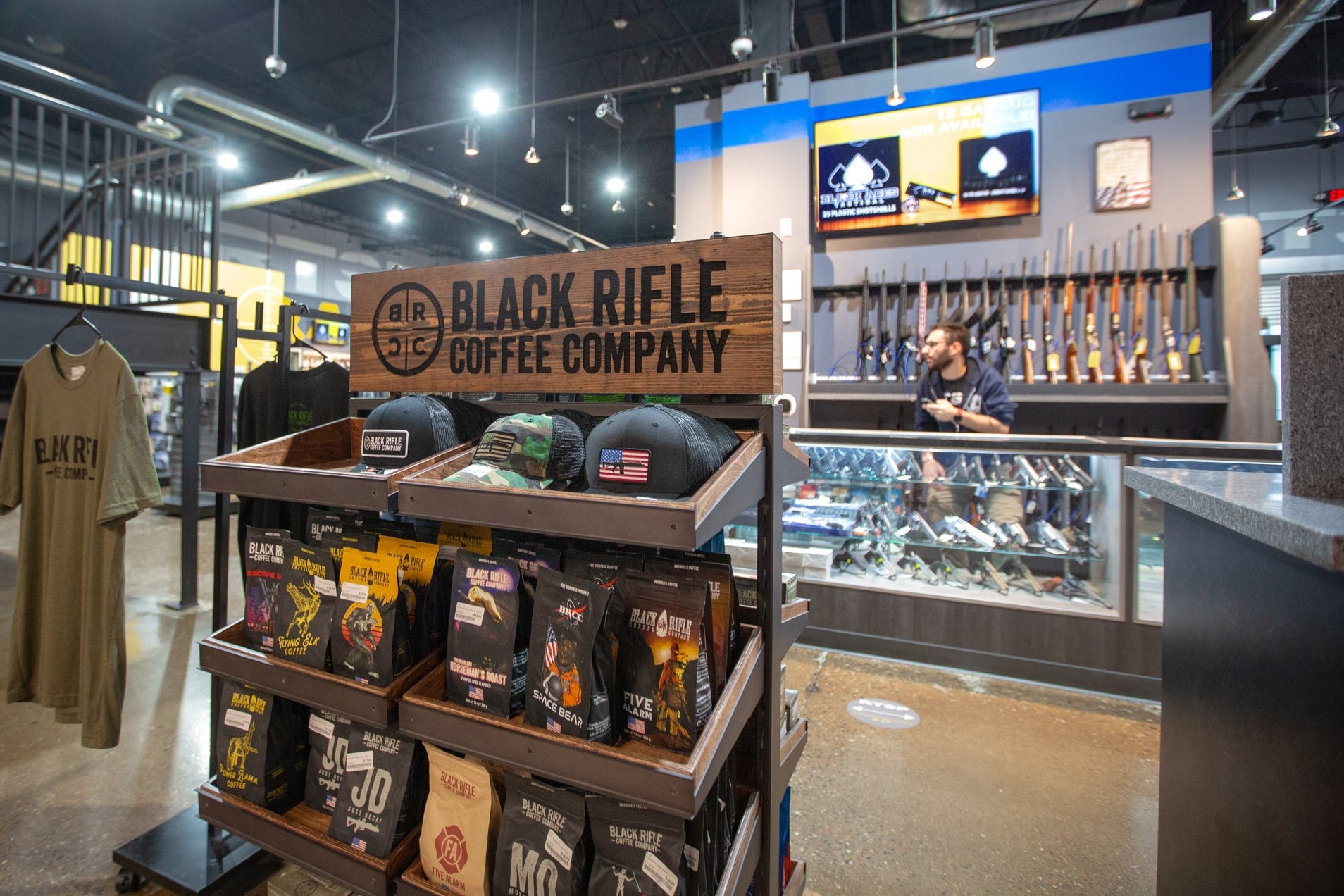 A shelf of Black Rifle Coffee products in front of glass display cases full of guns in a store