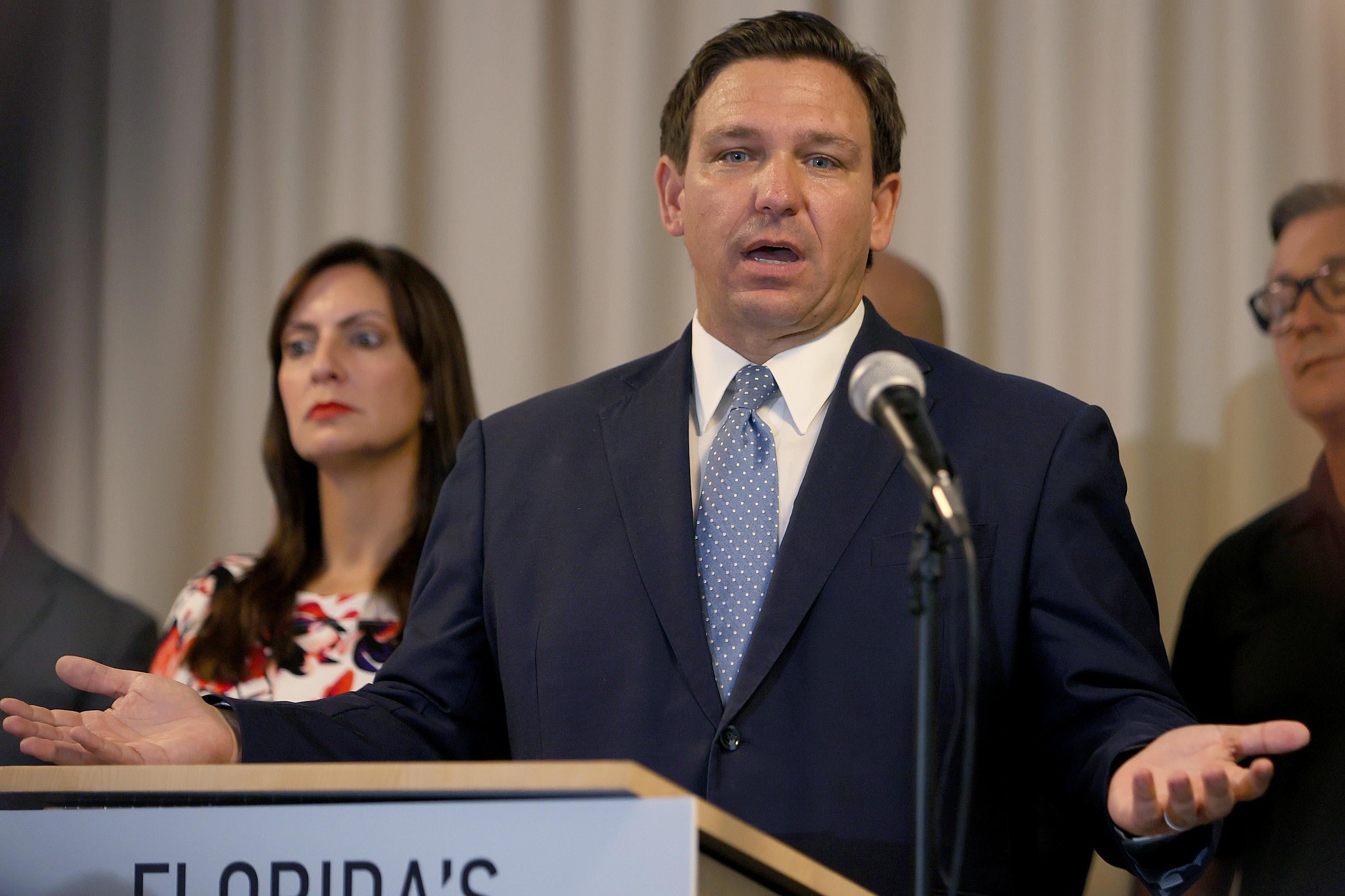 Ron DeSantis gestures as he speaks at a podium indoors