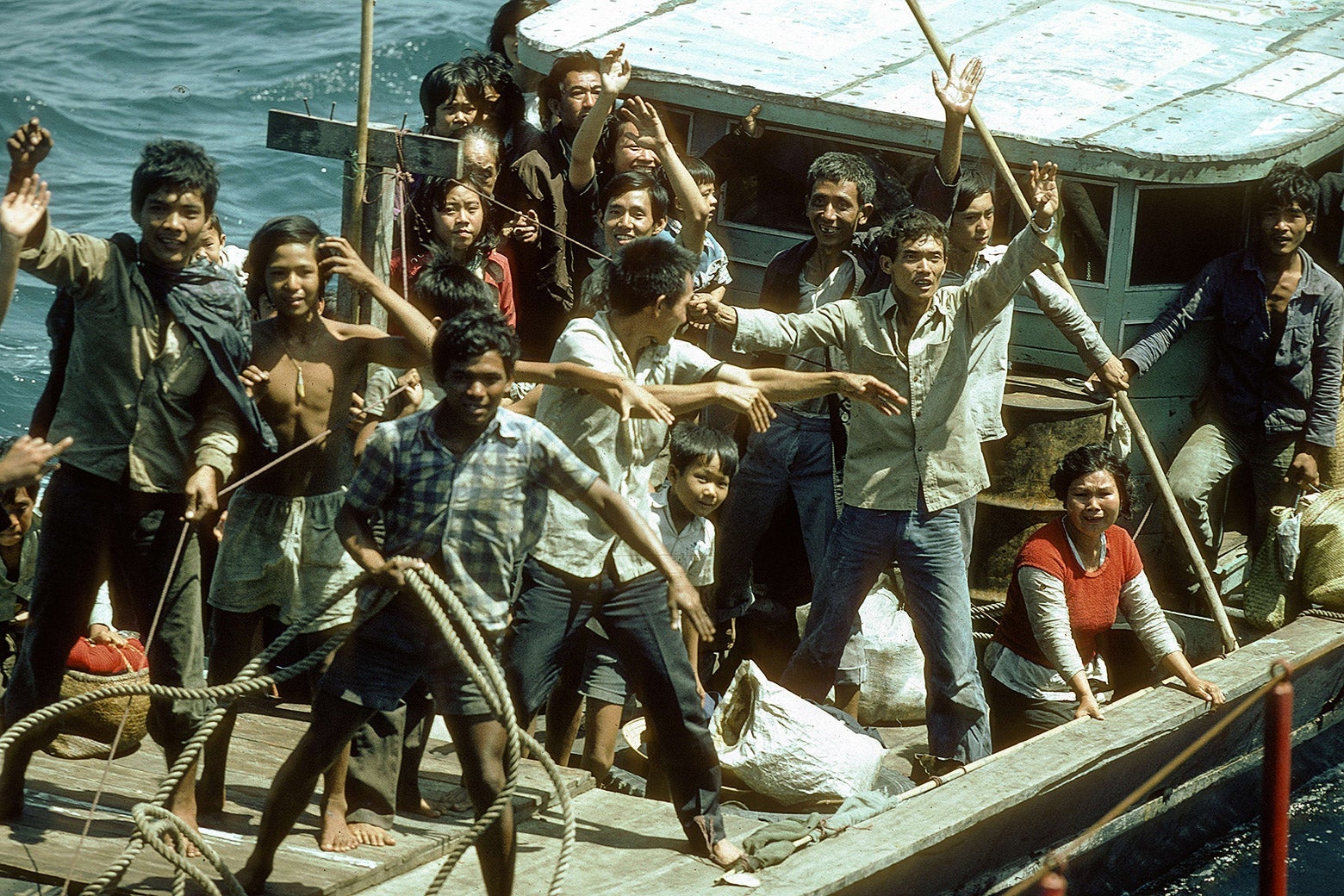 A group of Vietnamese boat people on board of their nautical vessel visibly happy to be rescued.