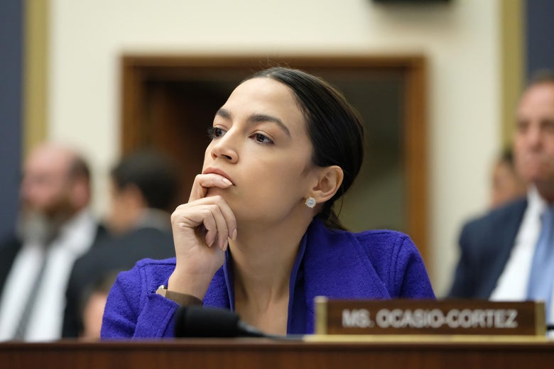 Rep. Alexandria Ocasio-Cortez listens with her hand on her chin.
