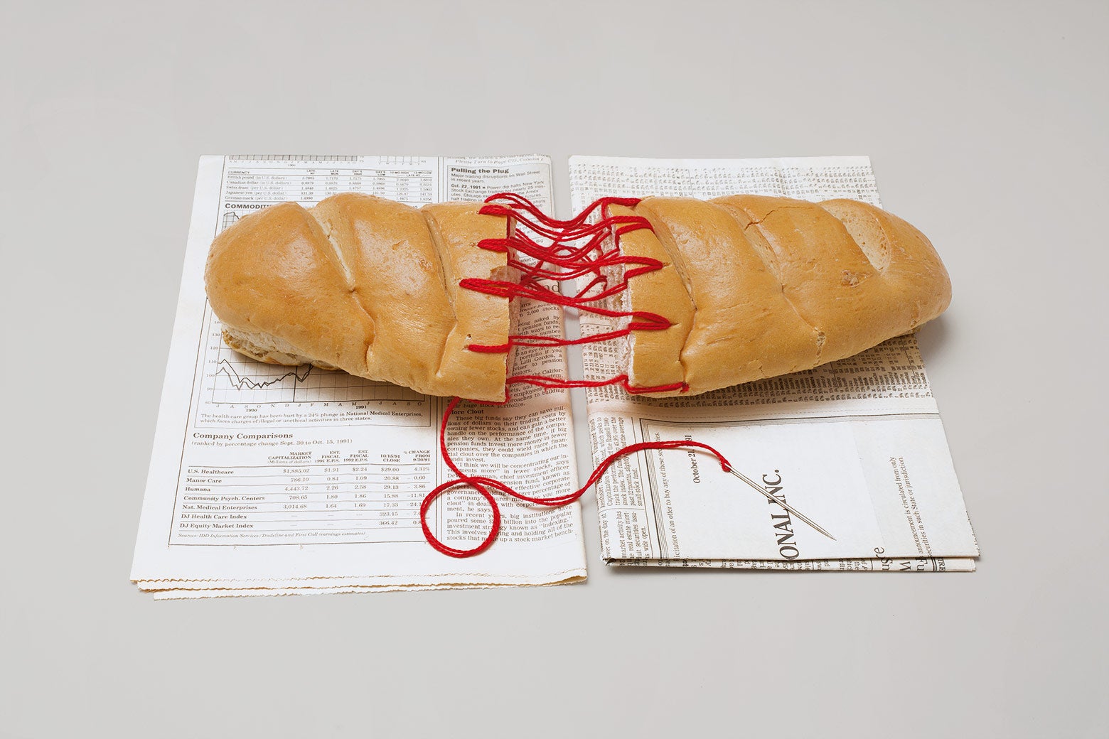 A sculpture of a loaf of bread stitched together with red string.