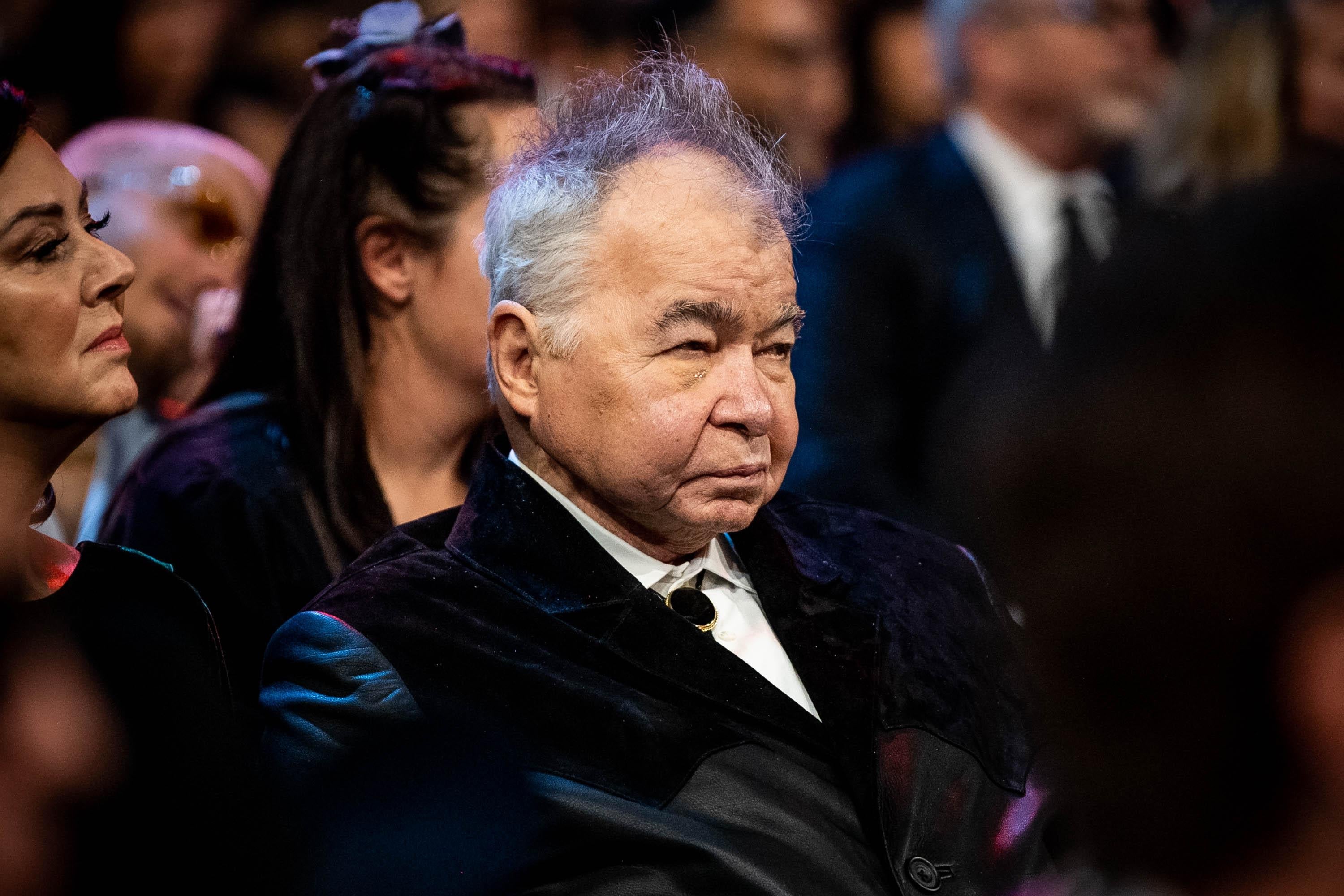 John Prine, in a velvet jacket and bolo tie, sitting in the audience at the Grammys.