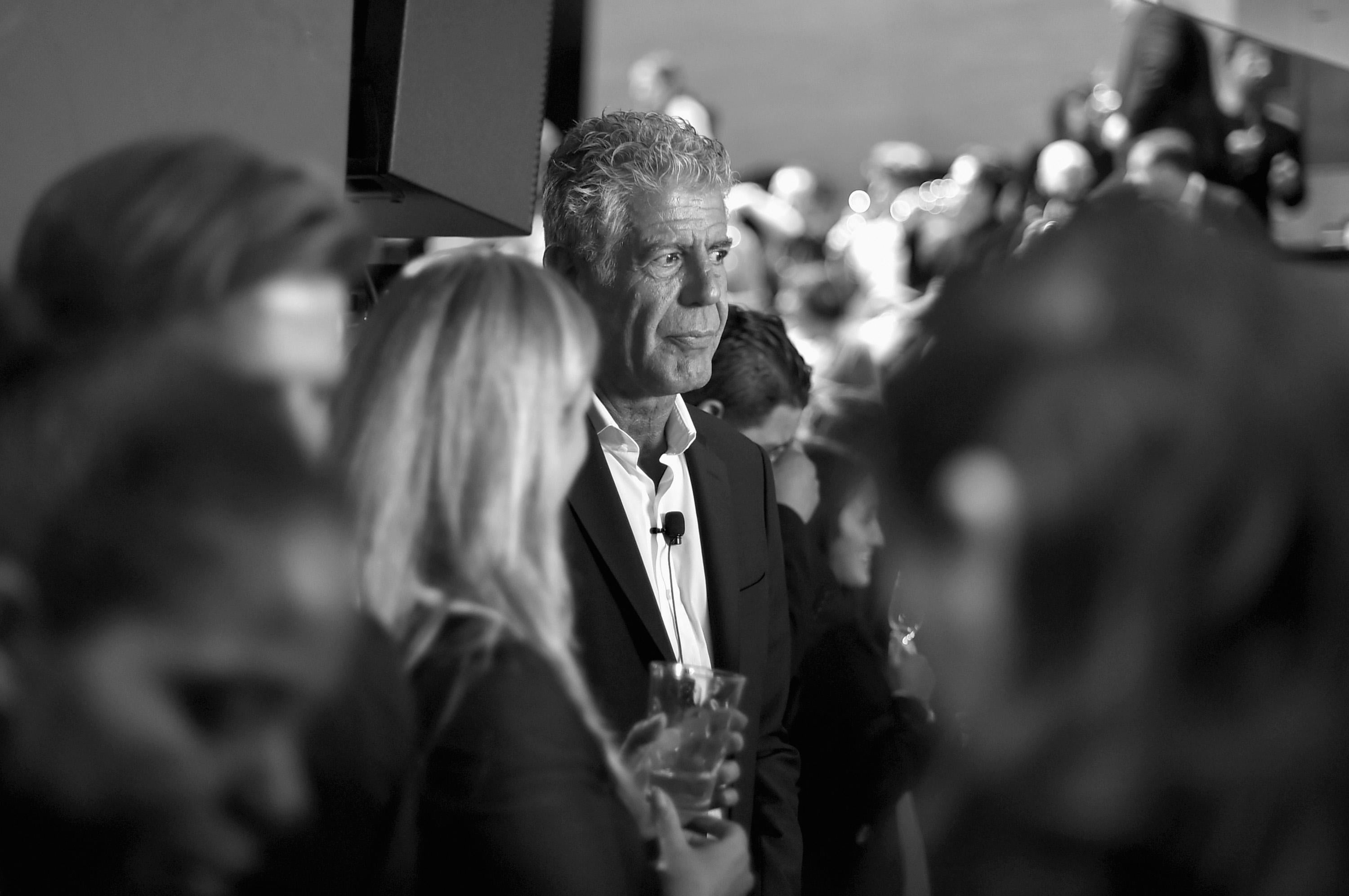 Black and white photo of Anthony Bourdain, standing out among a blur of other people, as he attends a screening of "Anthony Bourdain Parts Unknown: Japan with Masa" on November 7, 2016 in New York City.