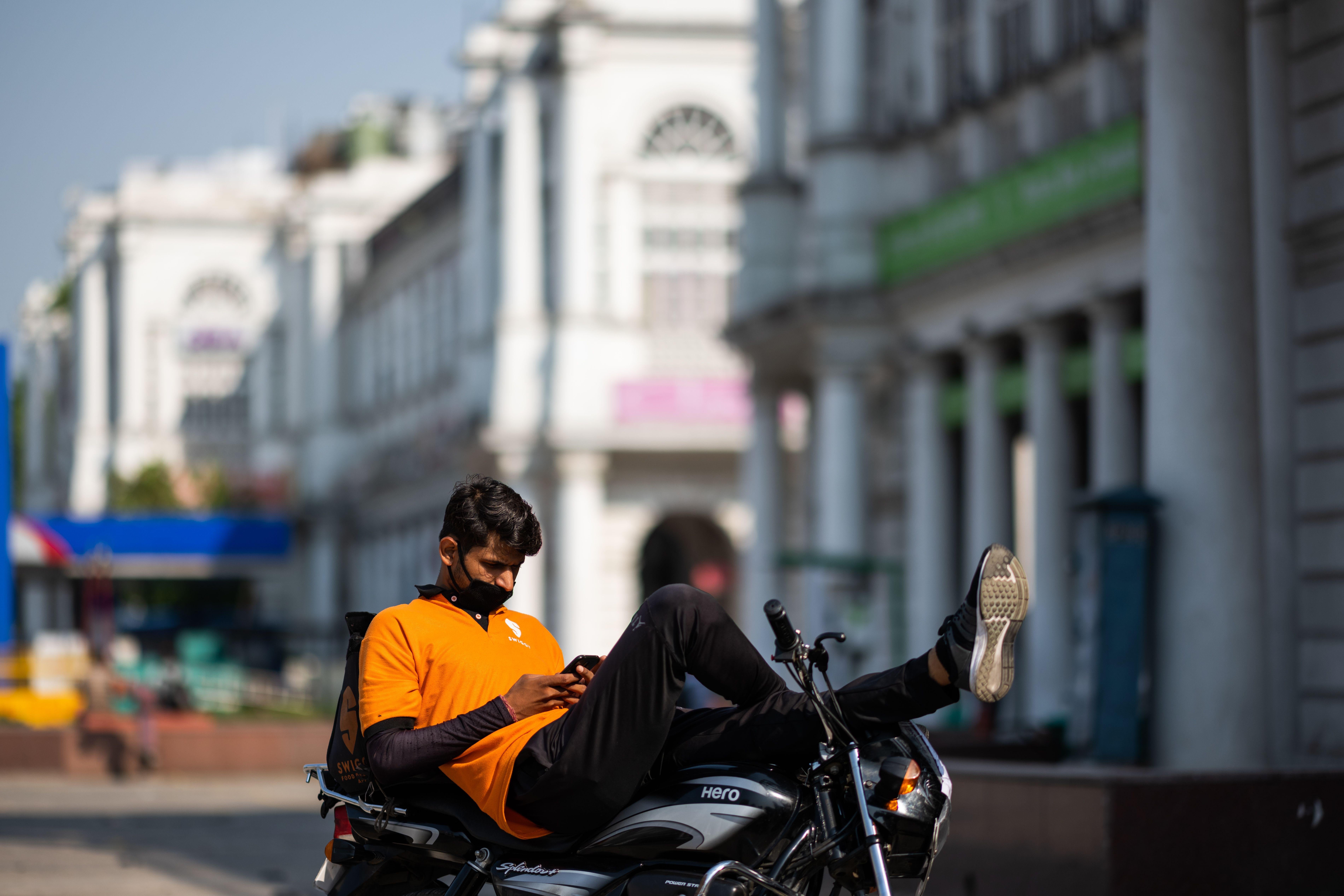 A man lounging on a stationary motorbike checks his phone.