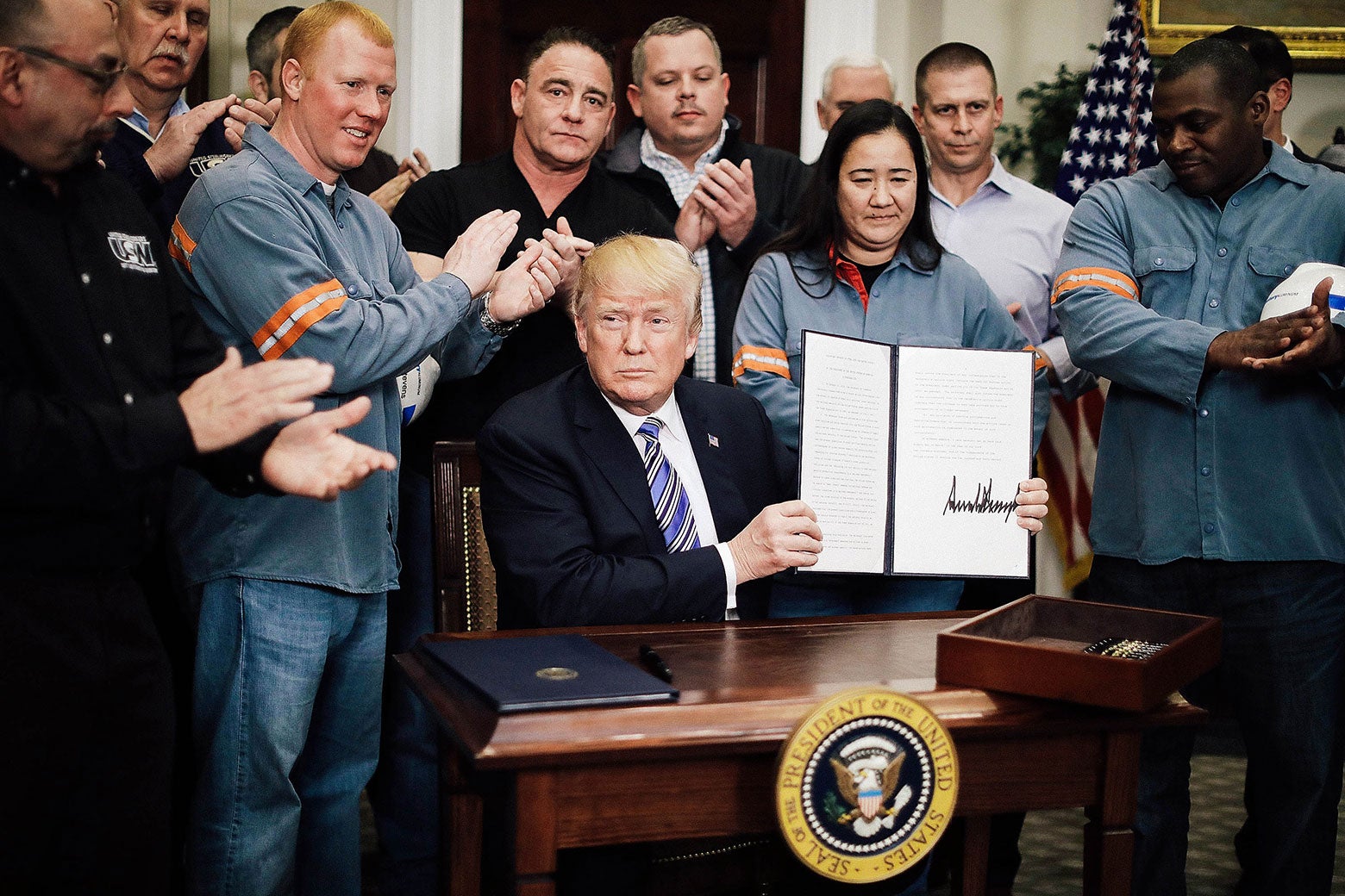 Surrounded by applauding steel and aluminum workers, President Donald Trump holds up the proclamation he signed.
