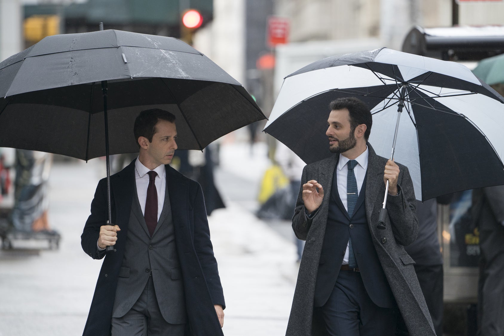 Kendall Roy and Stewy holding umbrellas, walking down the street.
