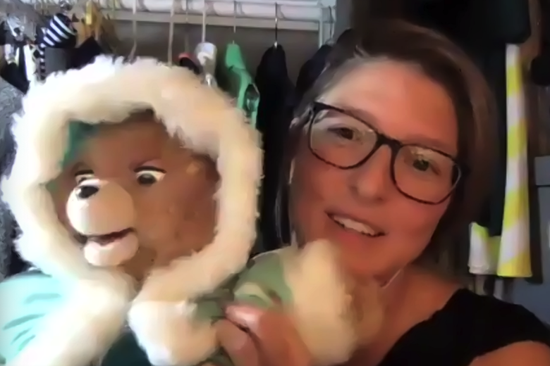 Elizabeth Newcamp holds up a Teddy Ruxpin toy that is wearing a blue coat.