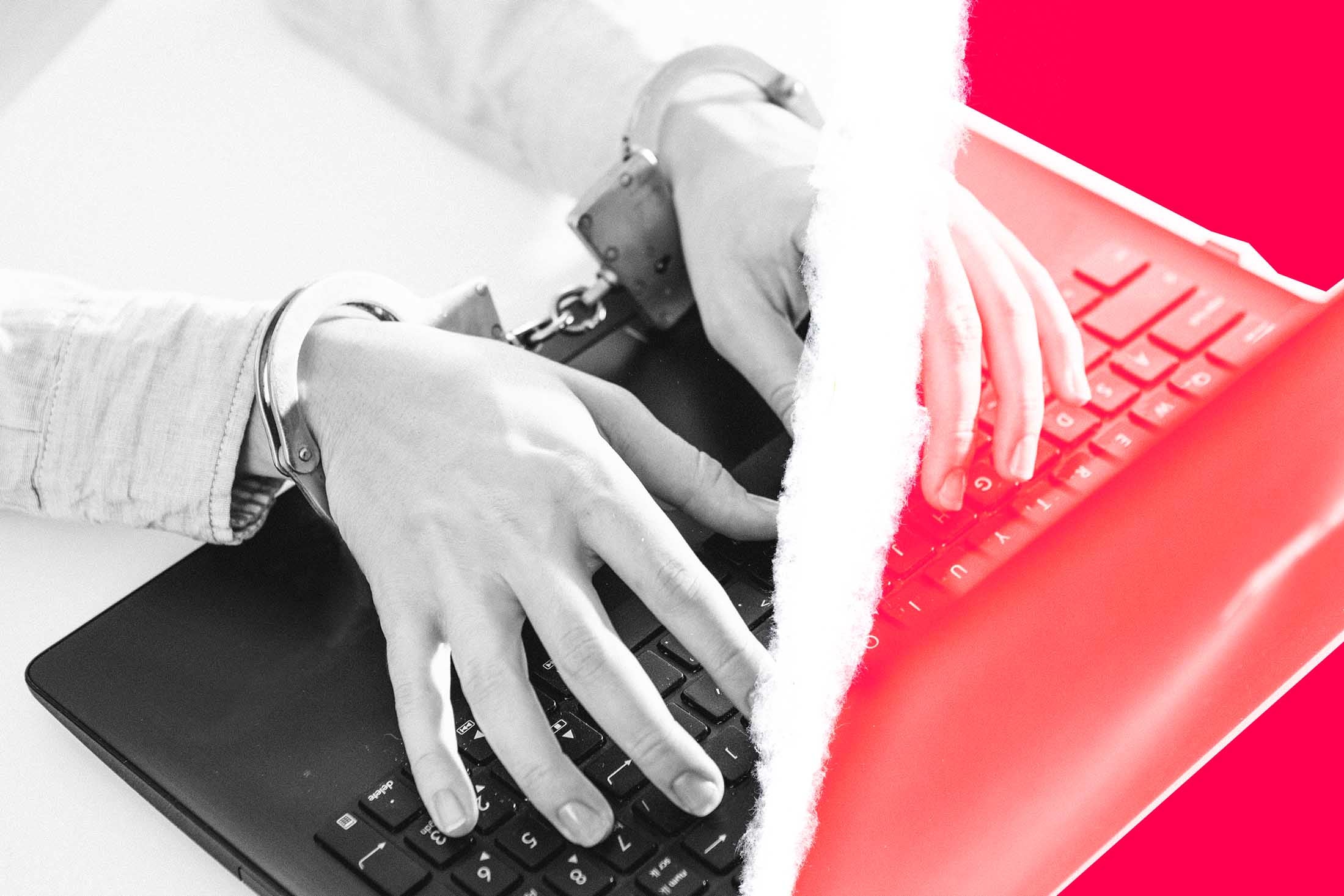 Photo illustration of handcuffed hands typing on a laptop, with a tear running through the center of the image.