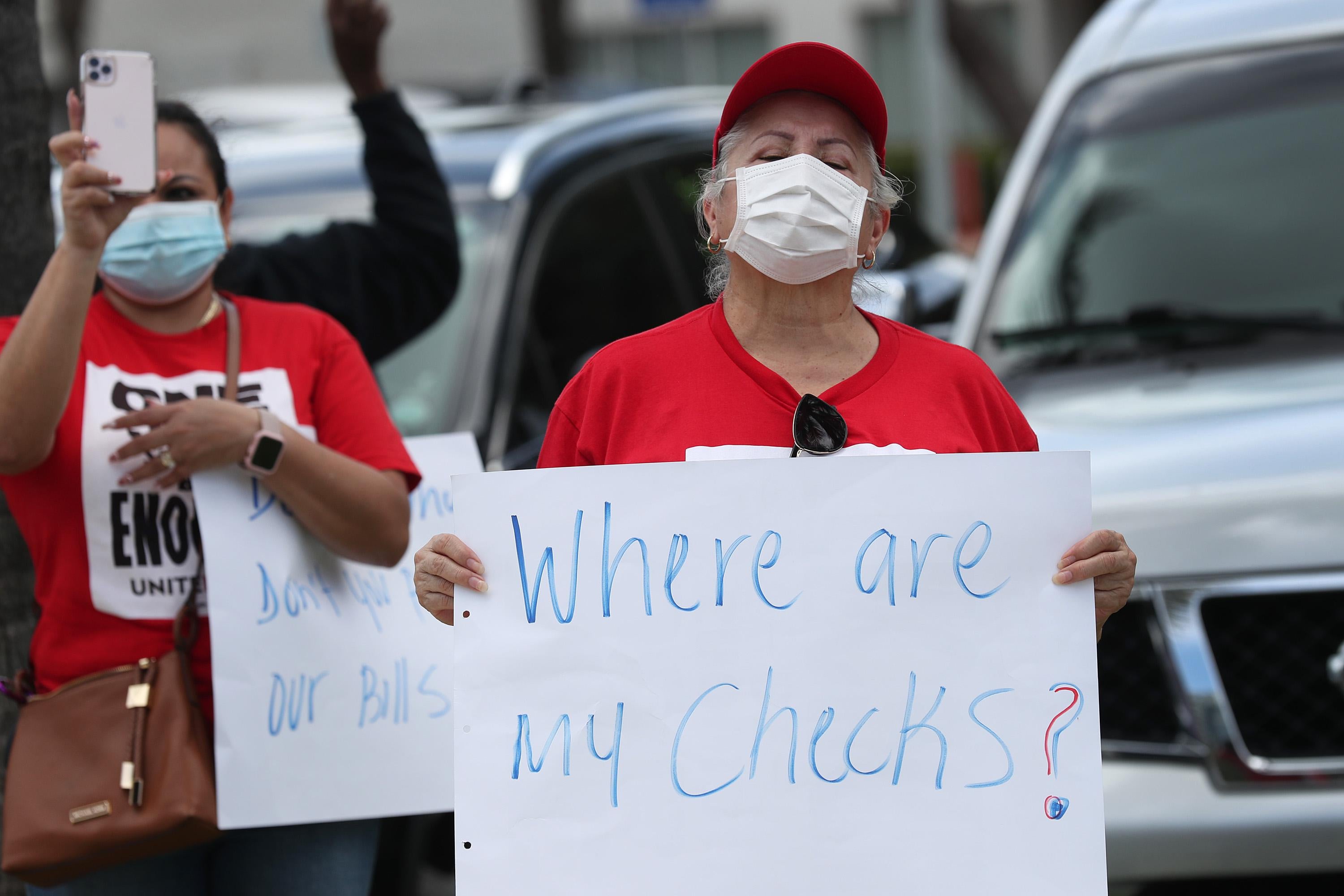 A protester in a face mask holds a sign that says, "Where are my checks?"