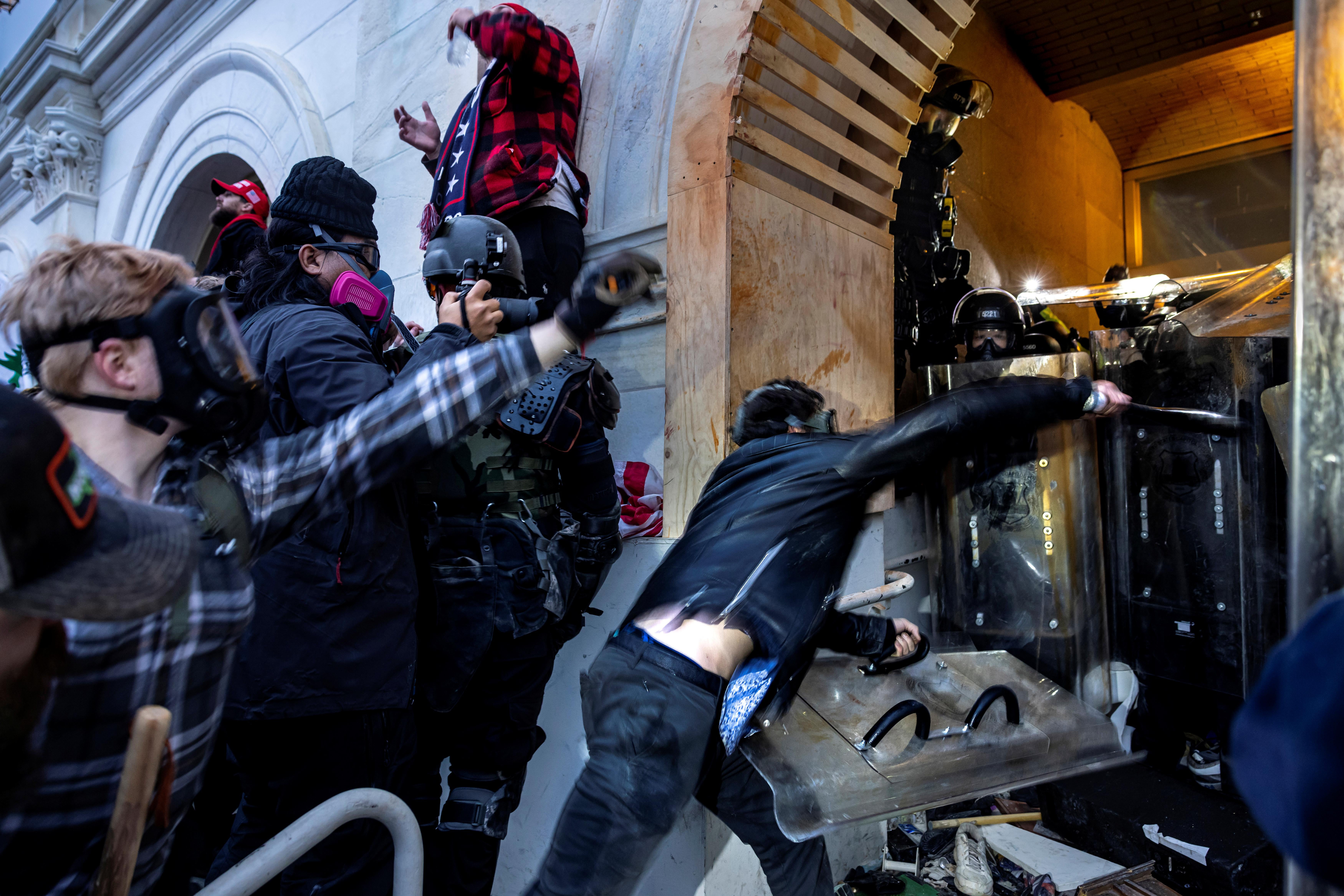 Trump supporters in tactical gear attempt to beat down a police barricade at an entrance of the Capitol on January 6