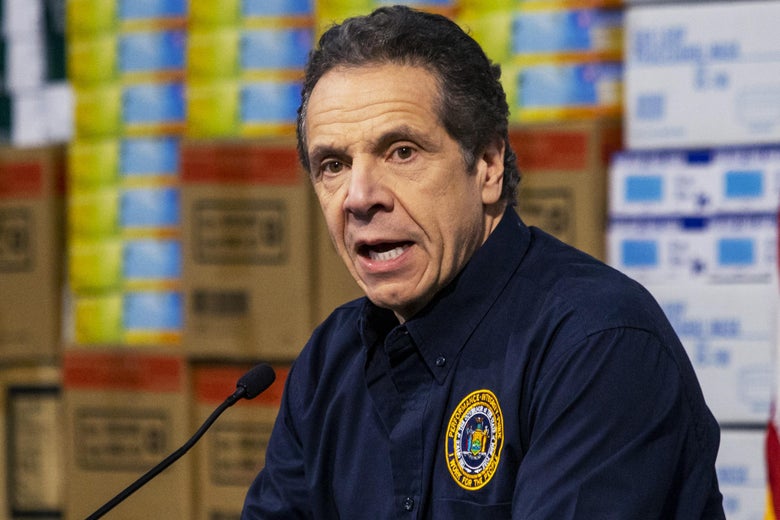 Cuomo speaks at a mic with boxes of supplies behind him