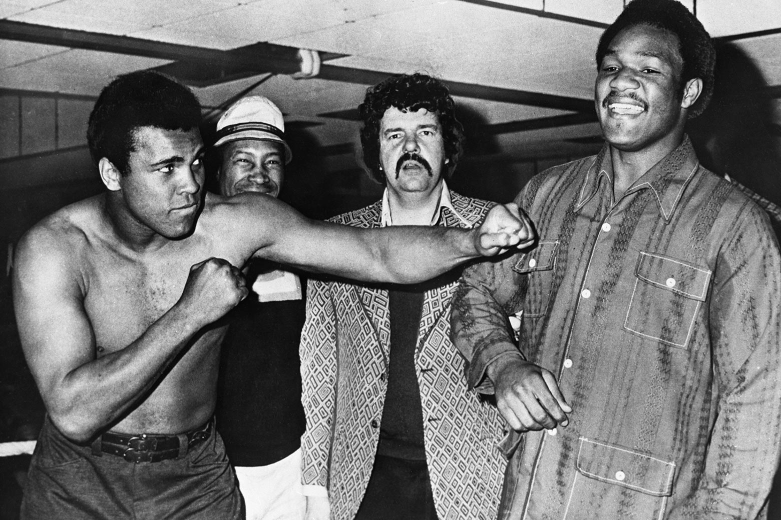A black and white photo in which world heavyweight boxing champion George Foreman, right, smiles disdainfully as former champ Muhammad Ali, left, goads him. 