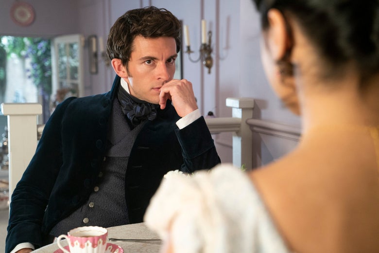 Jonathan Bailey sits at a table touching his lip, a teacup in the foreground.