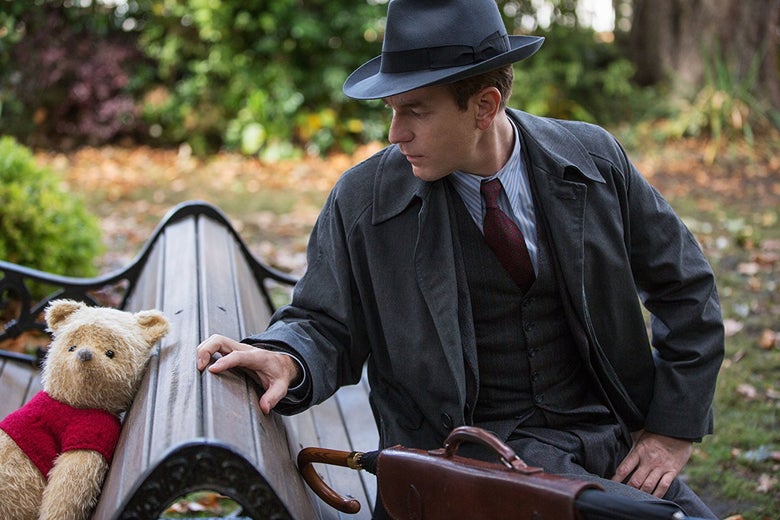 A CGI Winnie the Pooh sits on a live-action park bench, back to back with Christopher Robin (Ewan McGregor).