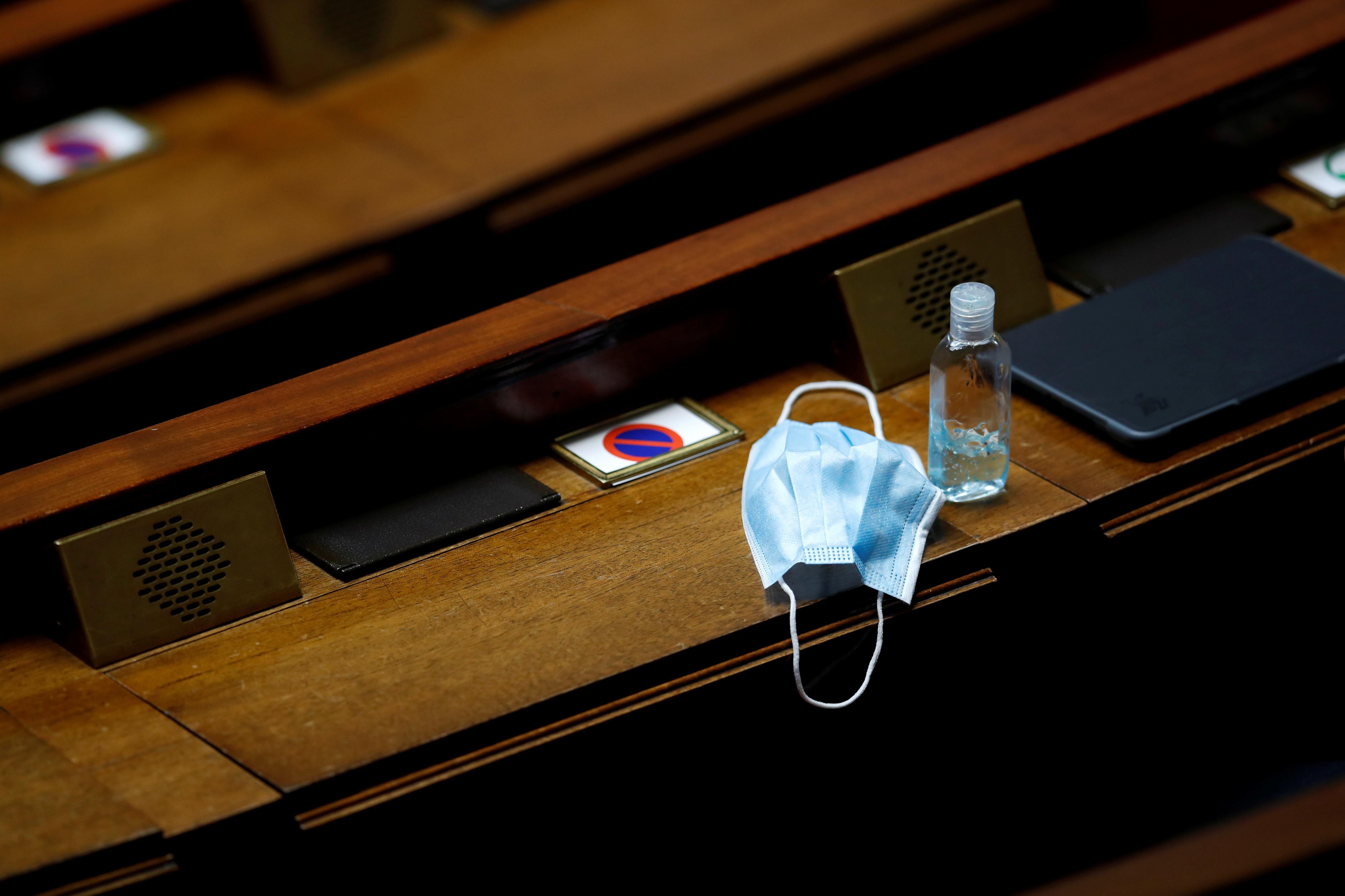 A protective face mask and a bottle of hand sanitizer sit on a desk.