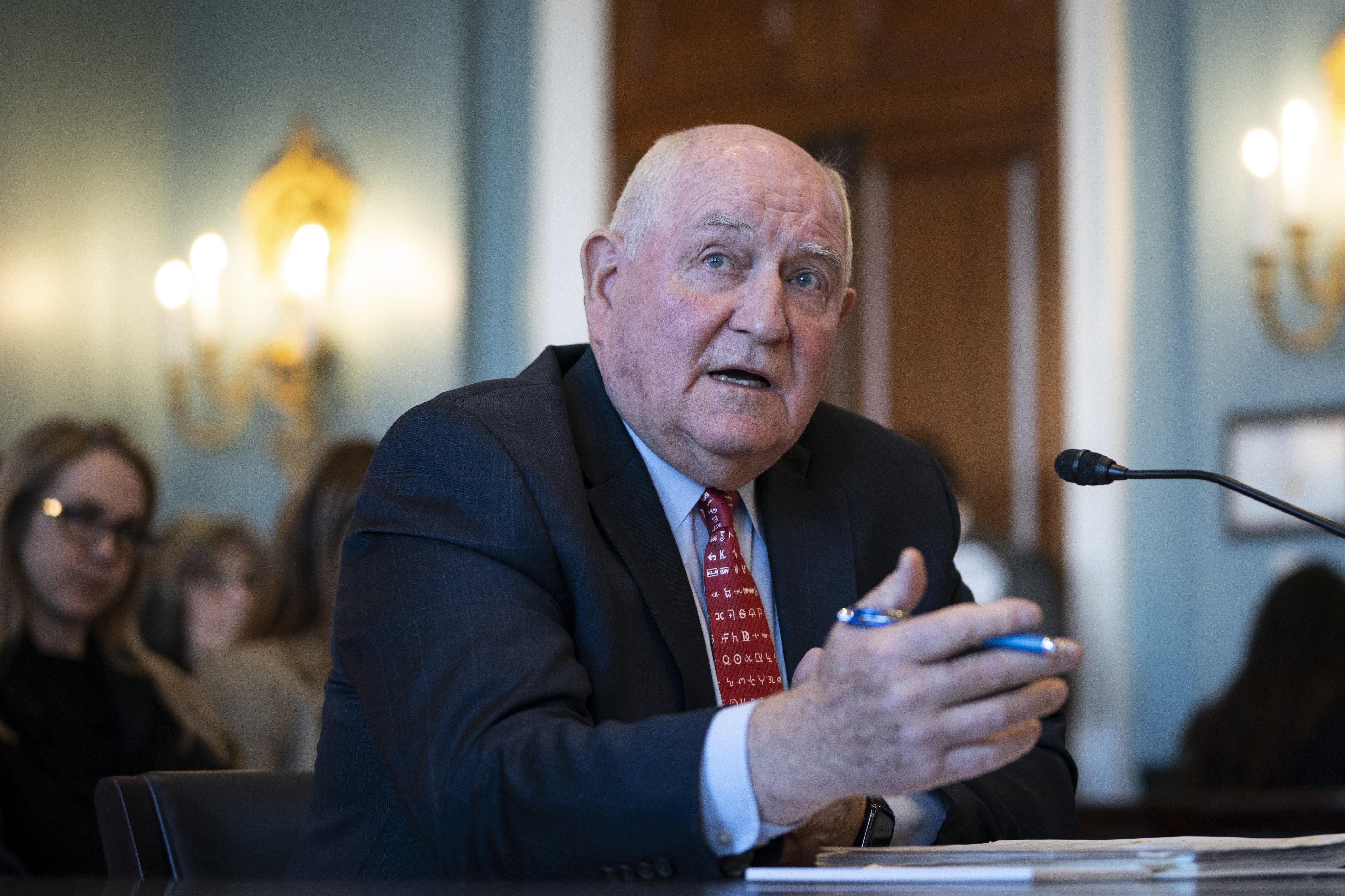 Sonny Perdue gestures with his hand as he speaks at a desk.