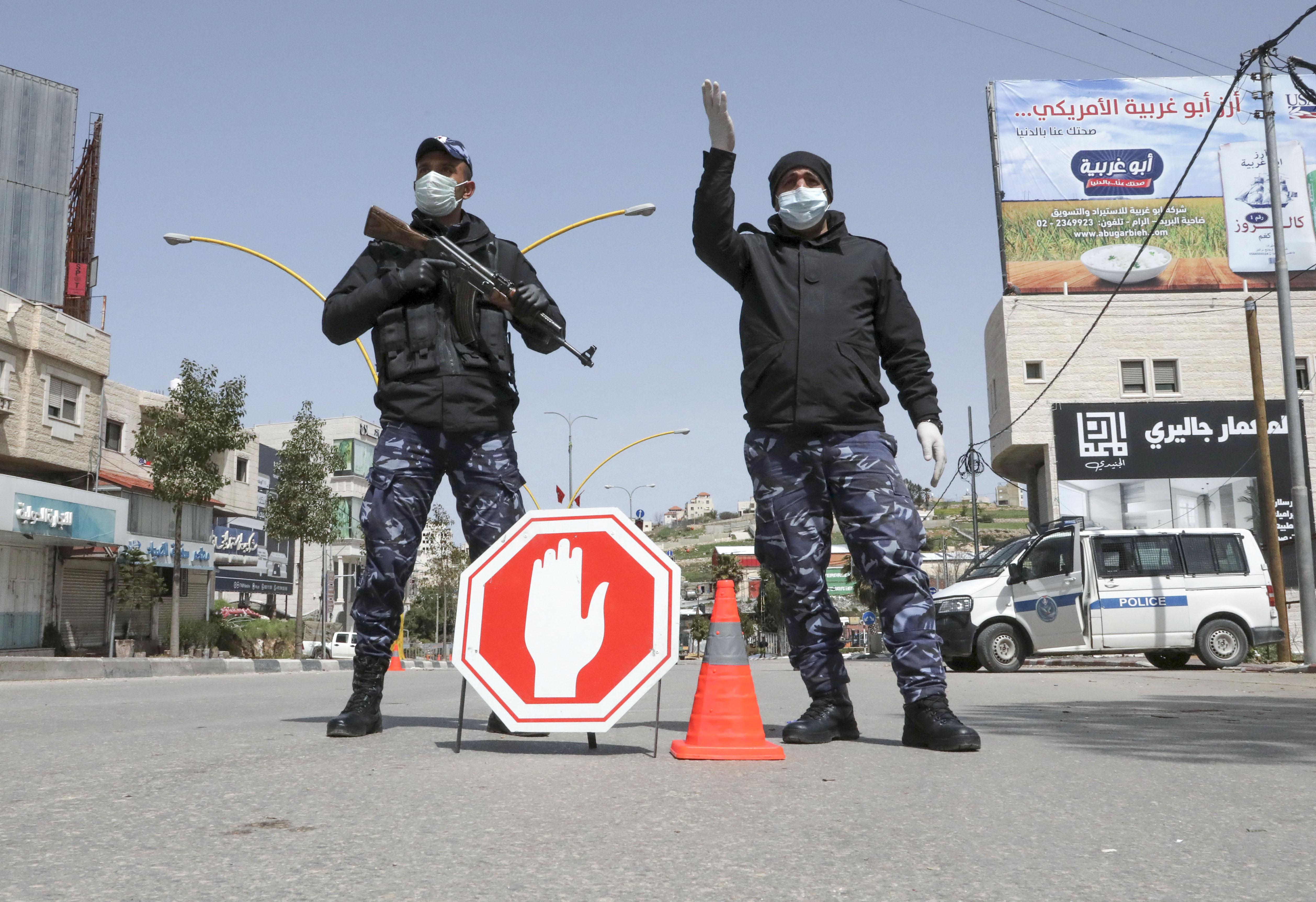 Two police officers wearing masks and carrying assault rifles man a checkpoint.