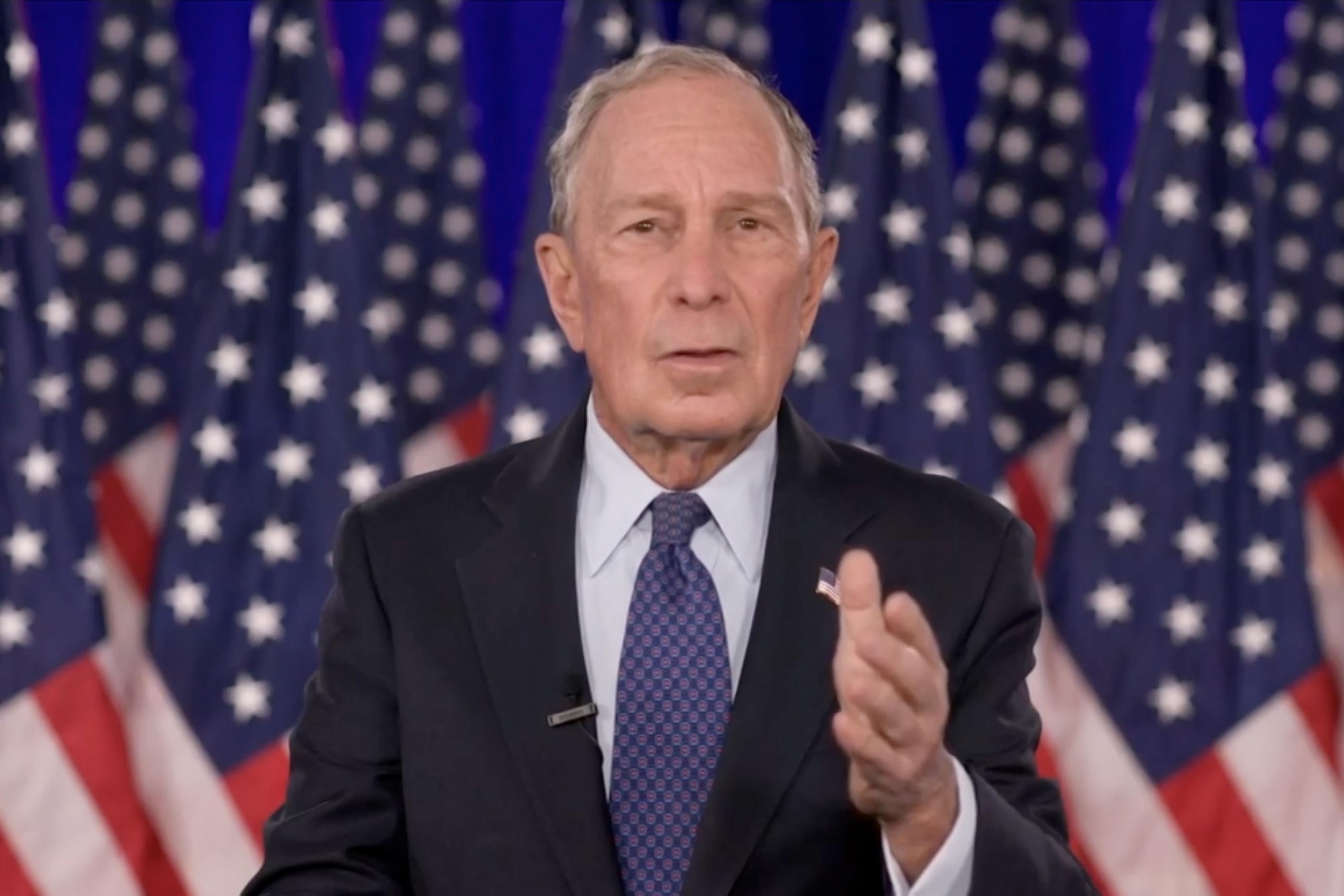 Michael Bloomberg, standing in front of American flags.