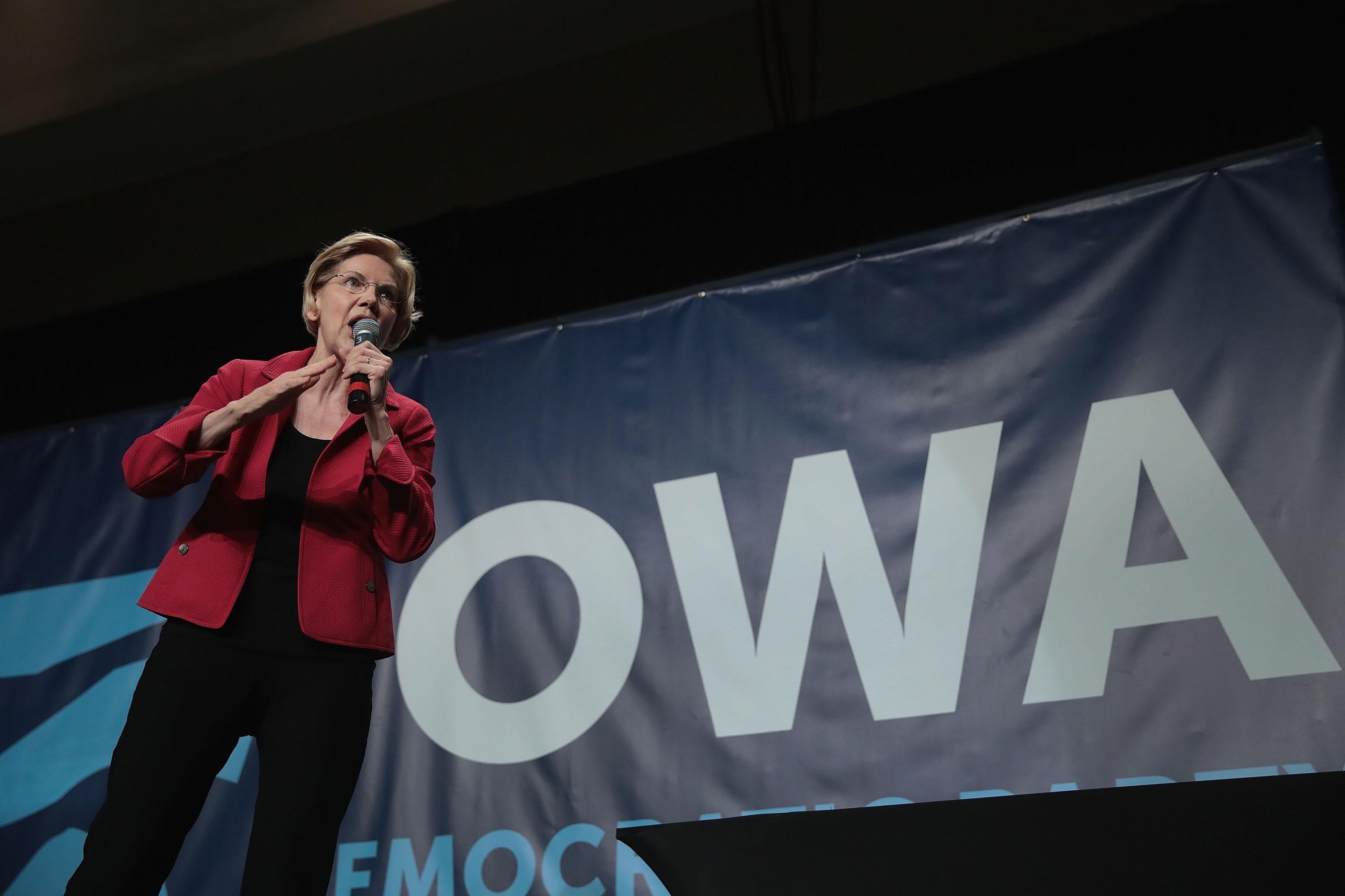 Elizabeth Warren holding and speaking into a mic onstage, campaigning in Cedar Rapids, Iowa.