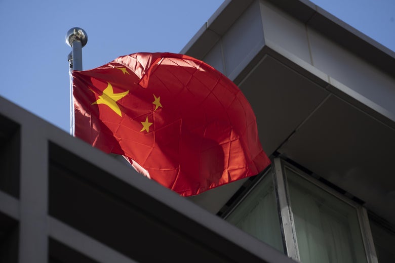 A Chinese national flag waves from the roof of a gray building.