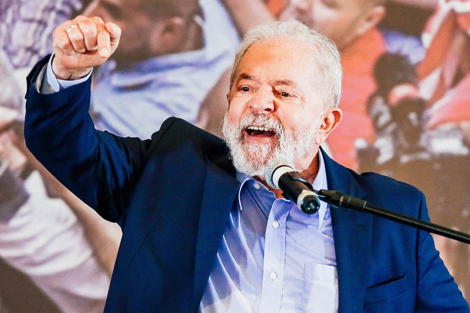 Lula raises his right fist as he speaks at a mic