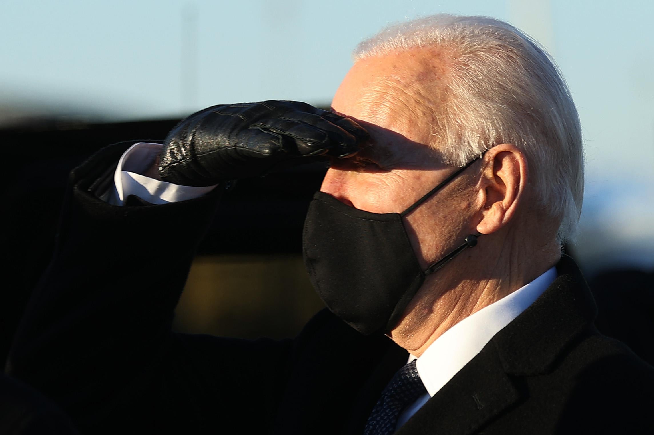 Biden, wearing a black mask, salutes with a gloved hand