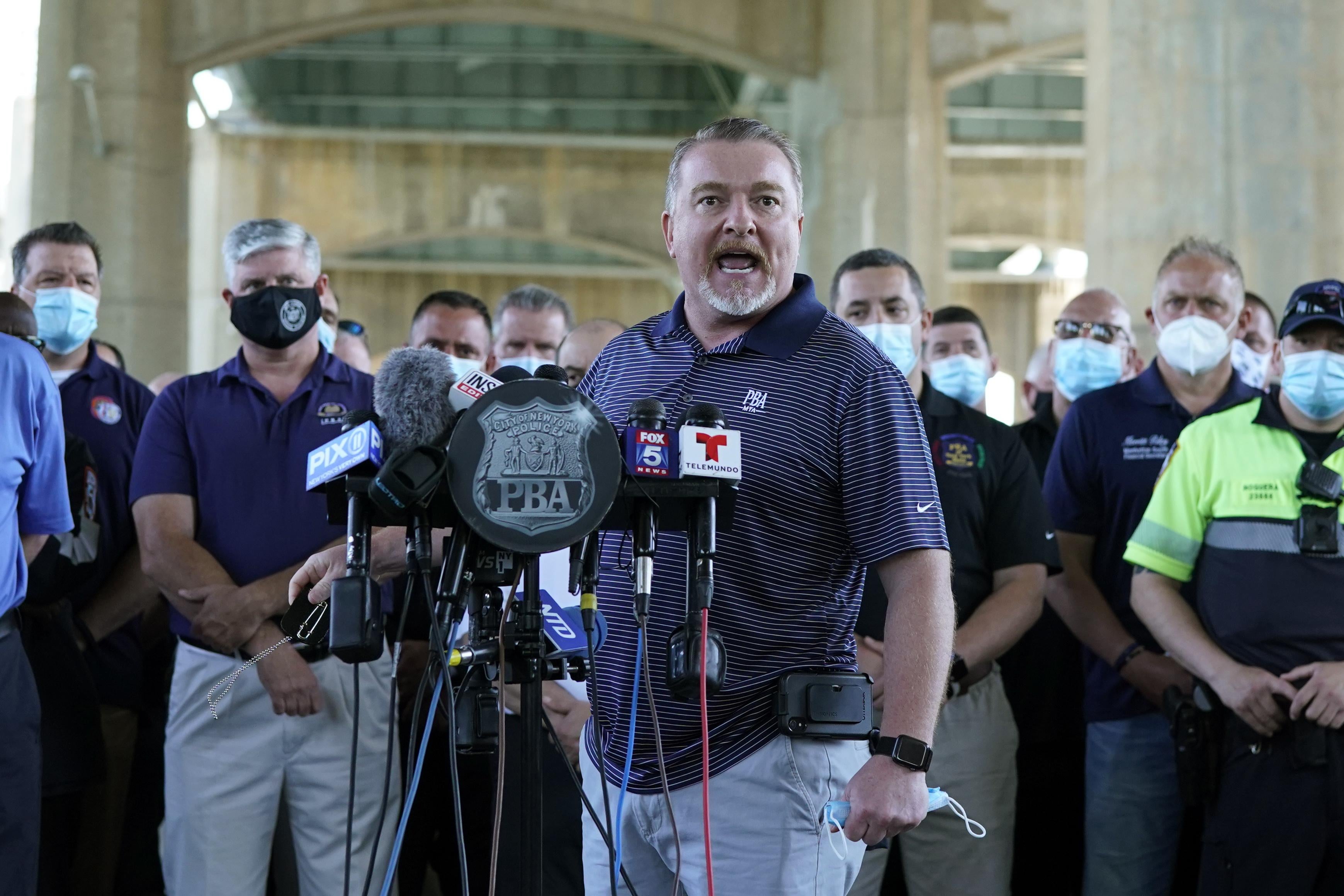 Mike O’Meara at a podium with microphones with law enforcement officers standing behind him.