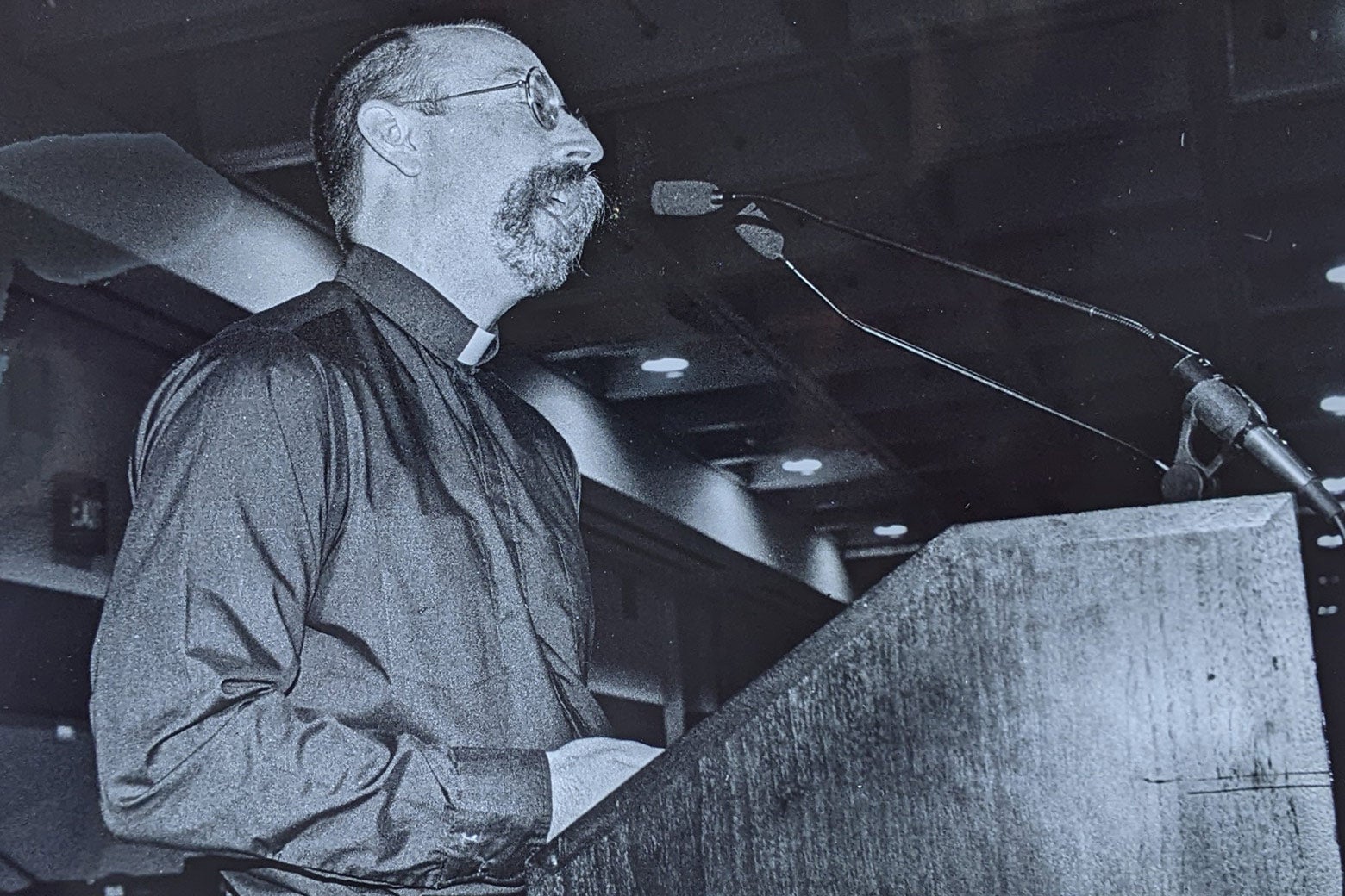 A middle-aged white man wearing glasses and preaching at a pulpit.