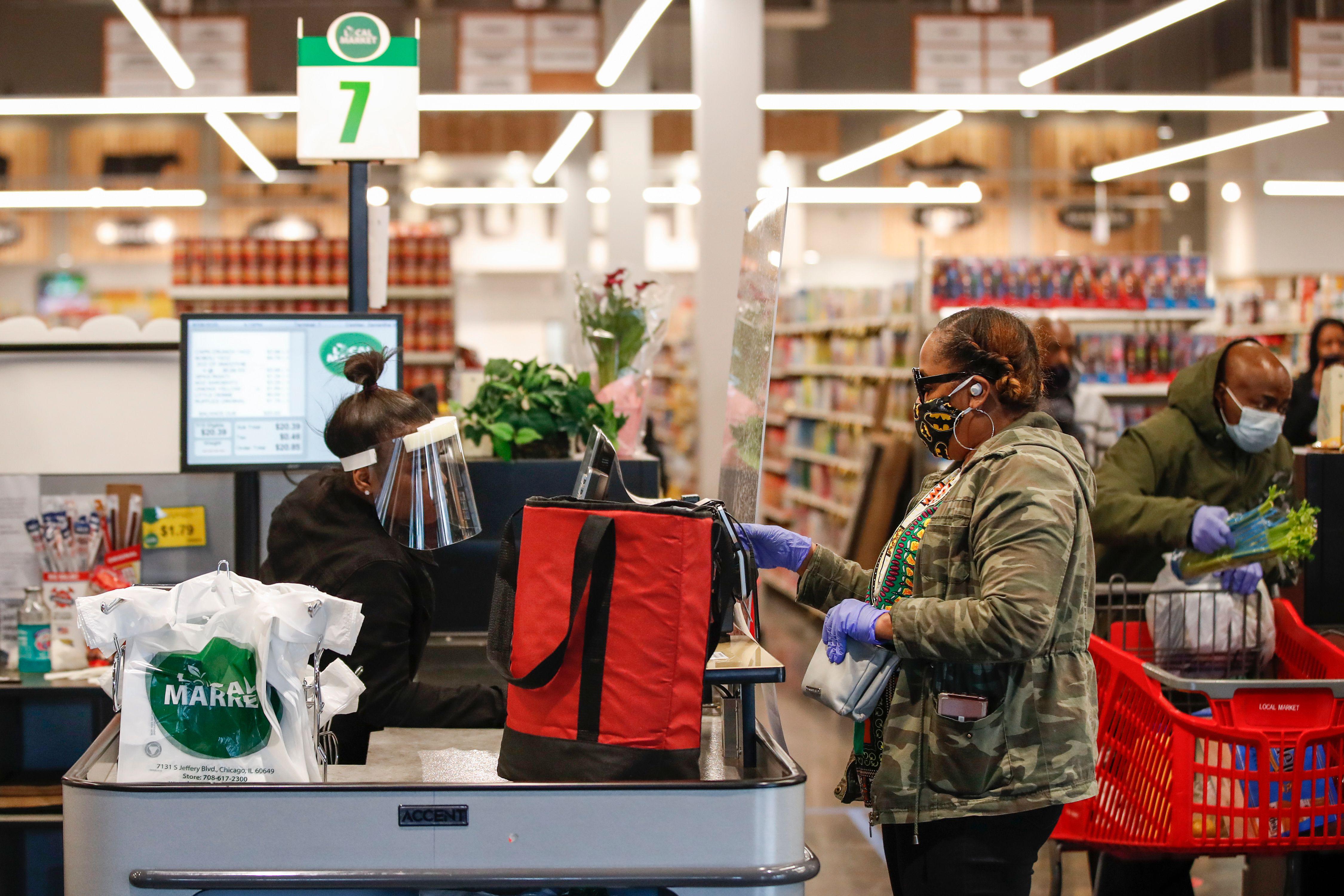 A customer wearing a face mask pays for her groceries at a store counter.