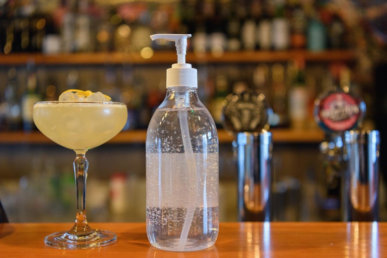 A bottle of hand sanitizer is seen between a cocktail and a beer tab.