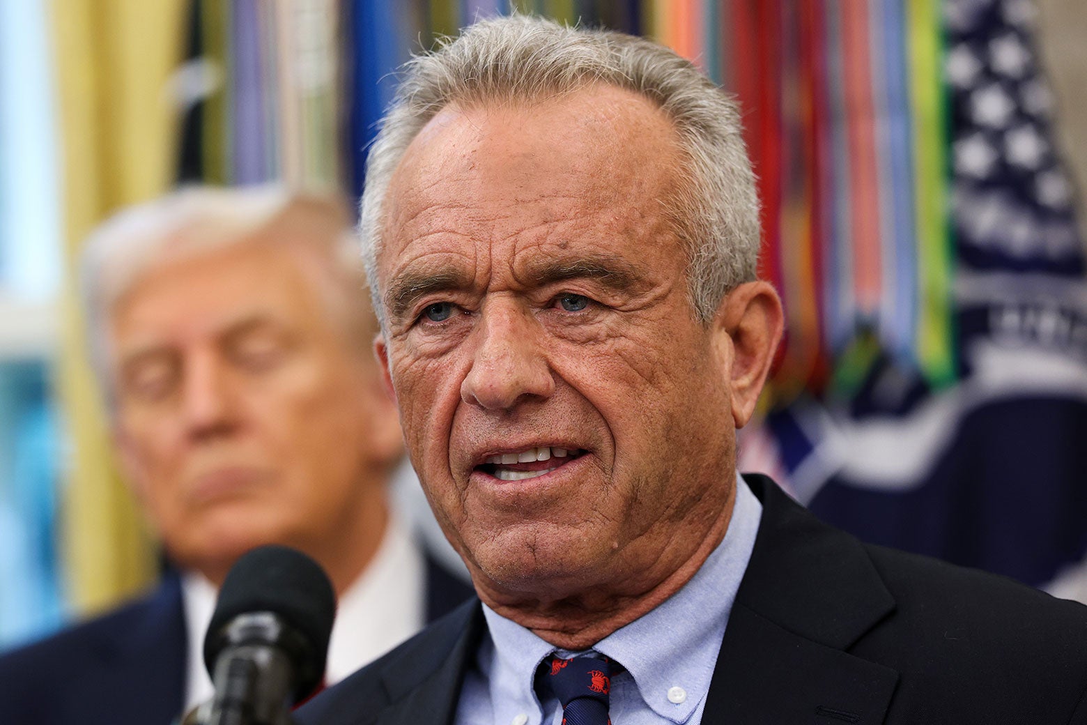 RFK Jr. vor einem Mikrofon, Trump hinter ihm.