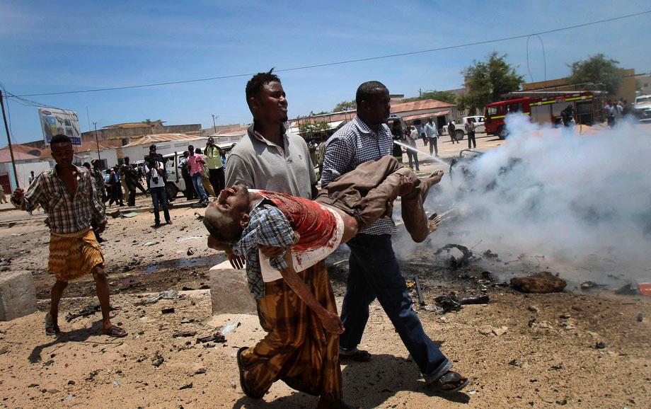 Somali men carry a seriously wounded man after a car bomb blast close to the Somali government's, headquarters in the capital Mogadishu, Somalia on Monday, March 18, 2013. An explosives-laden car that apparently was targeting a truck full of Somali government officials instead hit a civilian car and exploded, setting a nearby mini-bus on fire and killing at least seven people Monday, police and witnesses said.