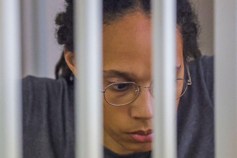 Griner wearing glasses, looking down at the ground from behind bars