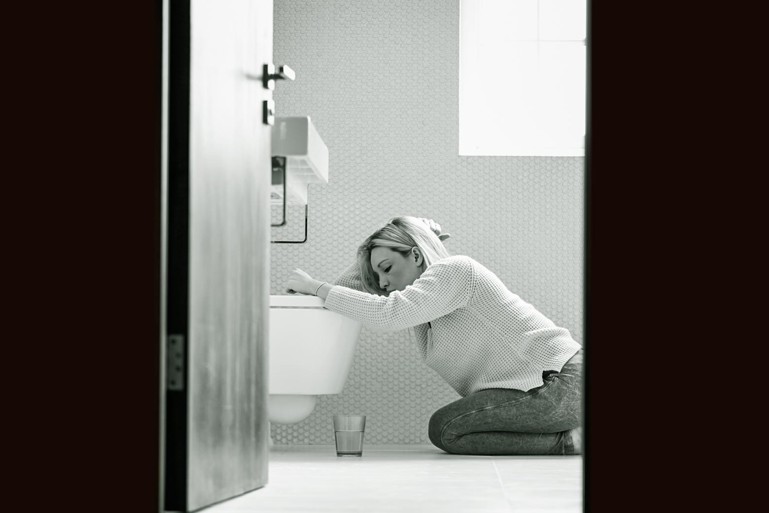 A woman kneels over the toilet in misery.