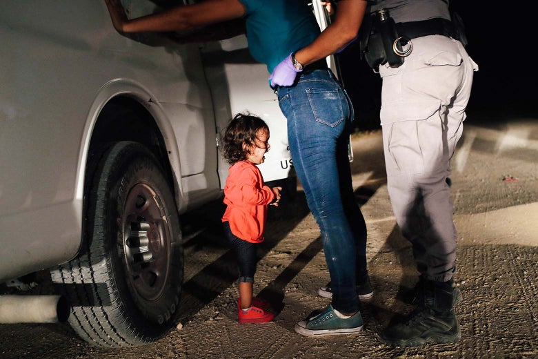 A Honduran girl cries on the ground as her mother is searched against a truck by a border patrol agent. 