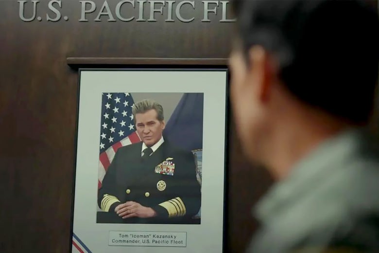 A photo sits framed in an honored place against a wooden wall, in it Val Kilmer as Iceman, his tips still frosted but his face aged. He's in a highly decorated Navy uniform. In front, the silhouette of a figure—presumably Tom Cruise, as Maverick—looks on.