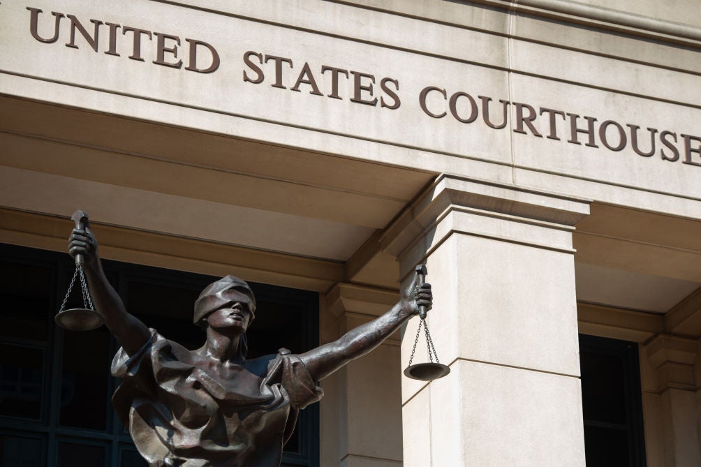 A blind-justice-holding-scales statue in front of a UNITED STATES FEDERAL COURTHOUSE sign.