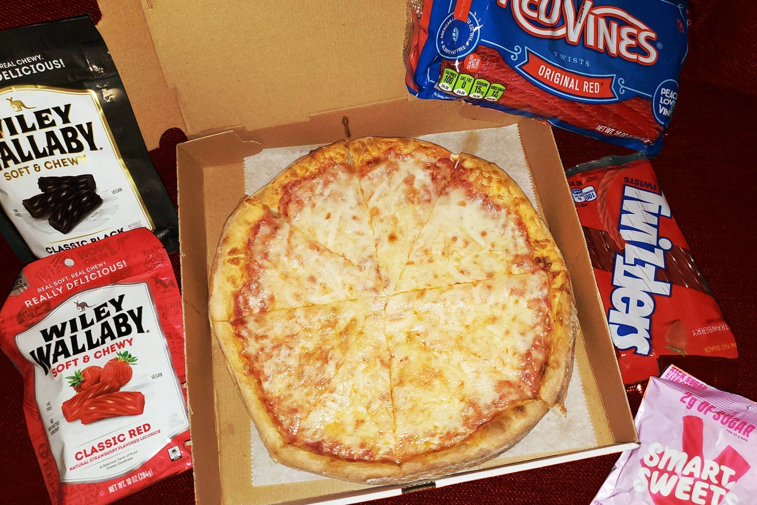 A cheese pizza in its box surrounded by bags of the licorice the author bought.