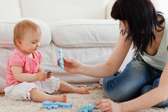 Woman and her baby playing with puzzle pieces while sitting on a carpet.