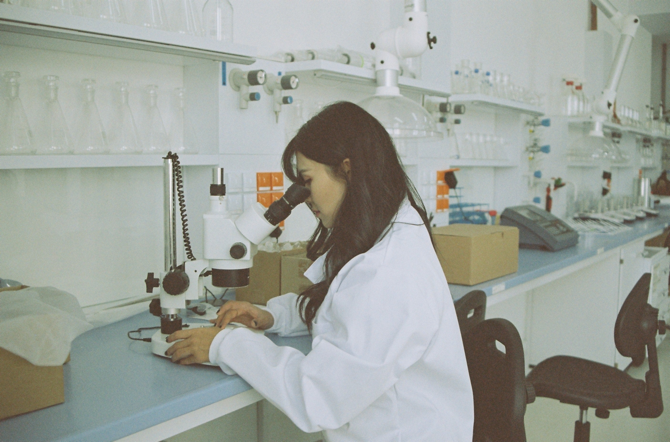 A woman in a lab coat looking into a microscope. 