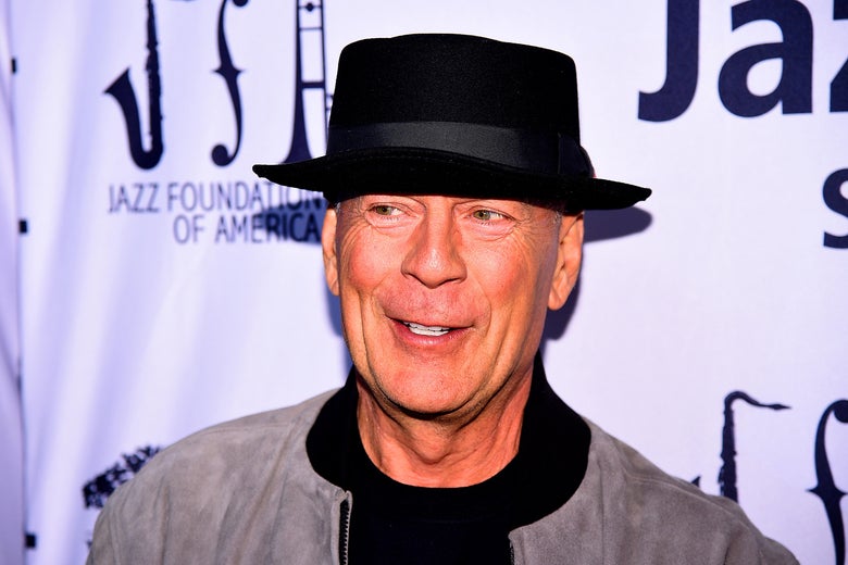 Bruce Willis smiling, in a black hat. 