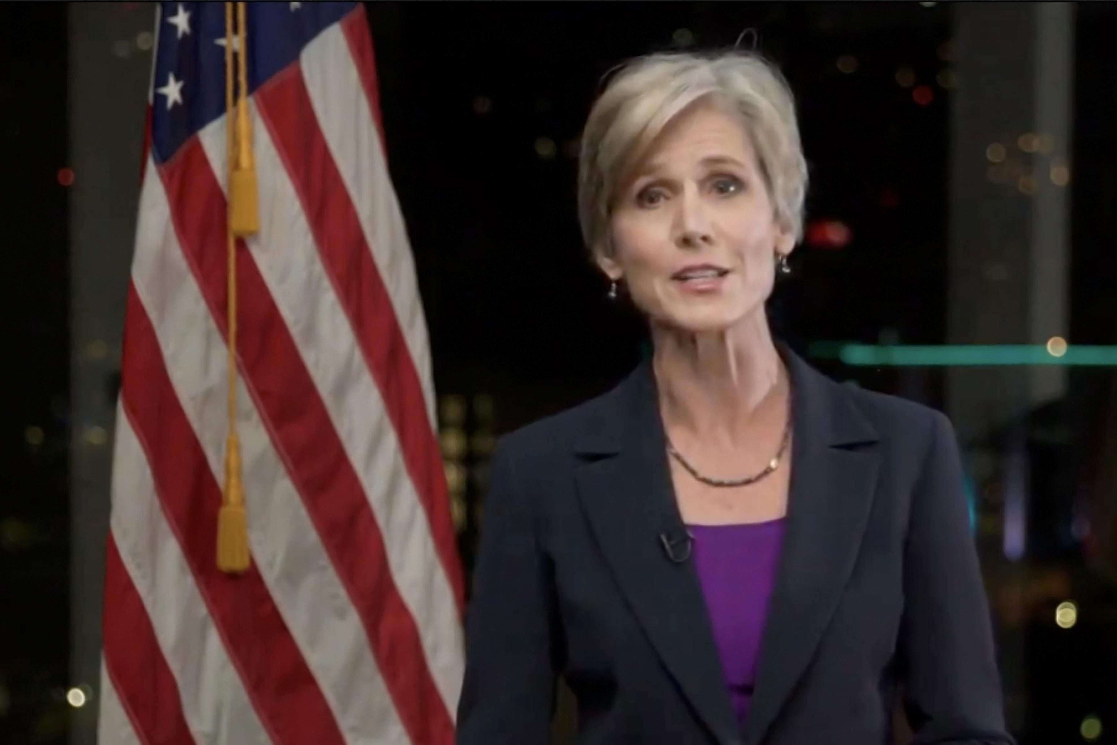 Yates speaks, standing in front of an American flag.