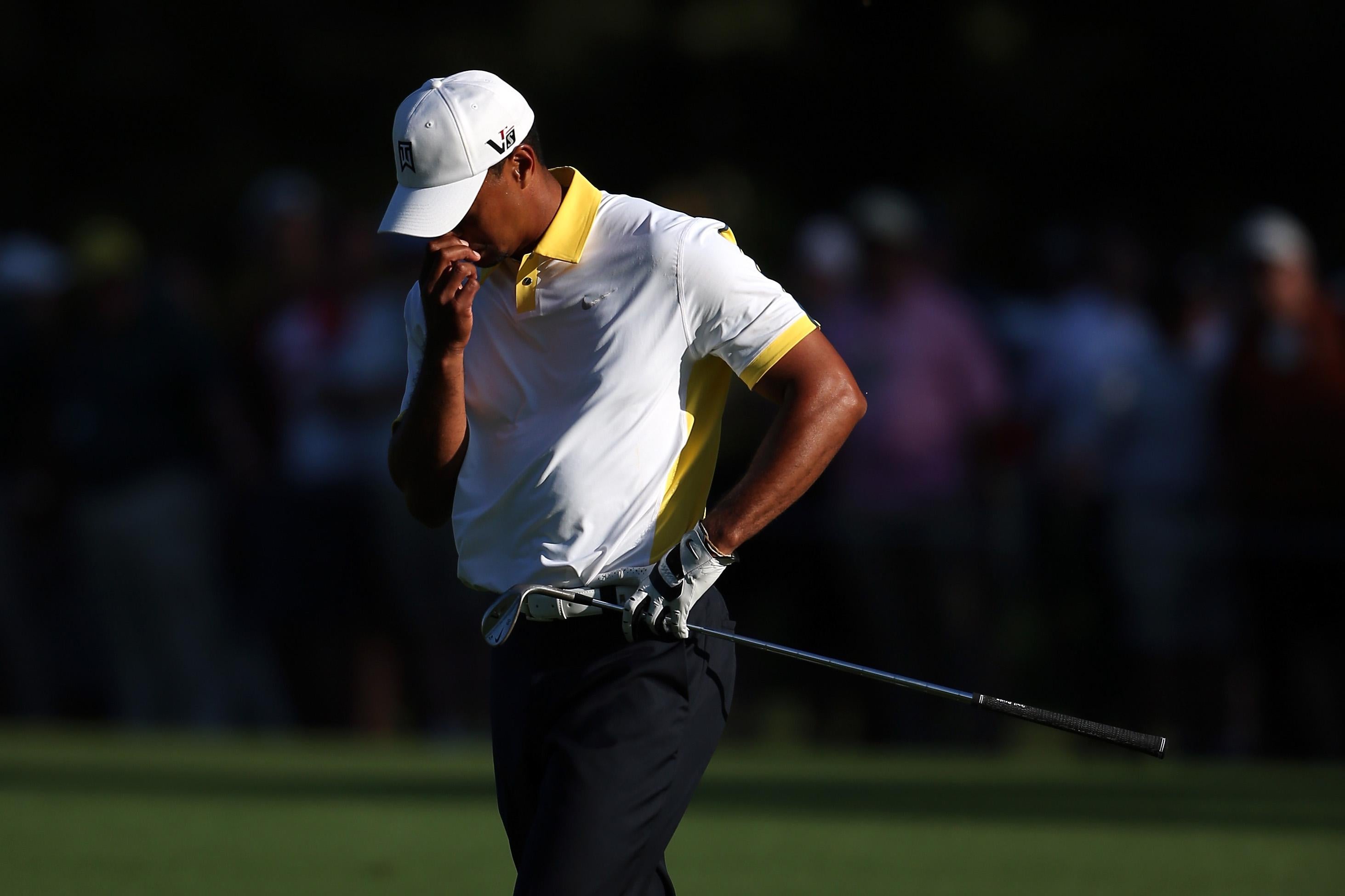 Tiger Woods holds his nose, closes his eyes, and points his head downward in disappointment