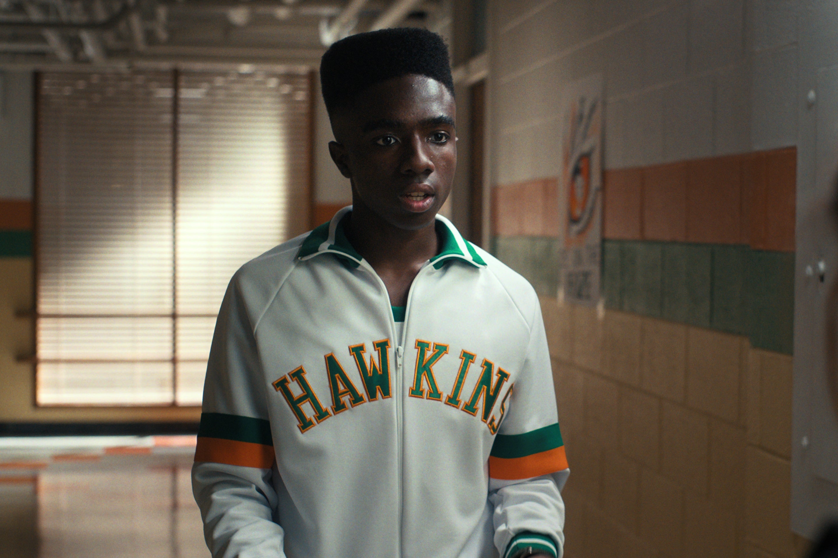 Lucas stands in a high school hallway wearing his basketball warmup jacket.