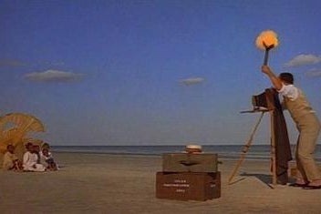 Using an old-fashioned camera, a man takes a picture of a family on the beach.