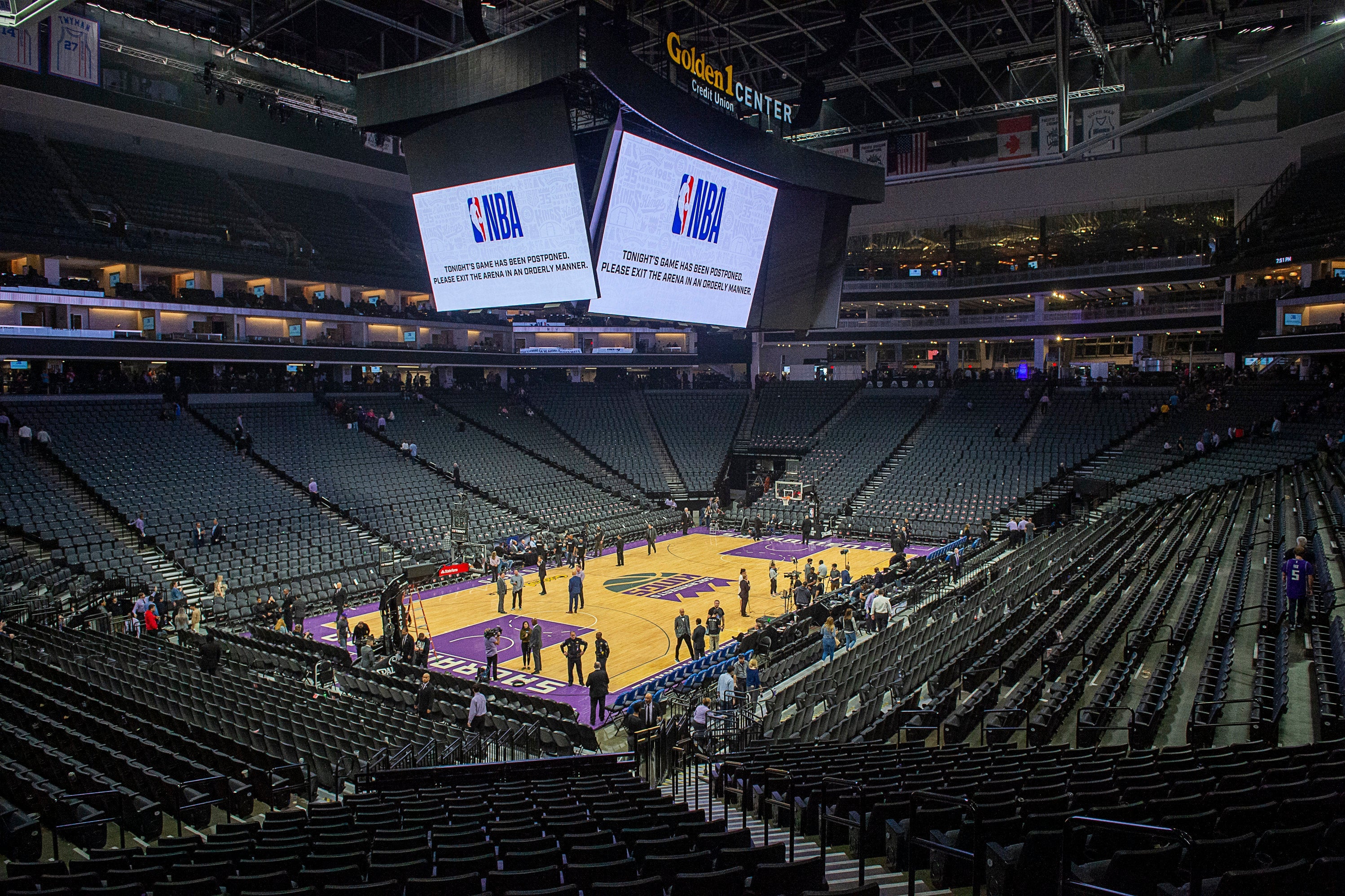 A near-empty basketball court with a Jumbotron overhead broadcasting the NBA logo.