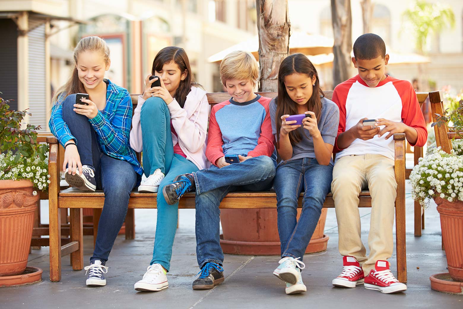 Kids sit on a bench and look at their smartphones.