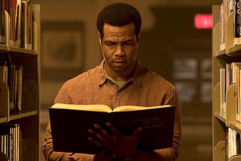 Isaiah Mustafa holding a book in a library in It: Chapter Two.