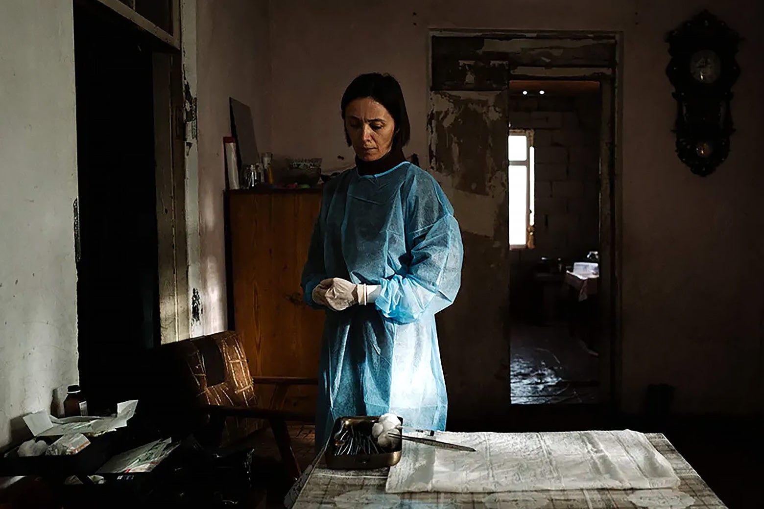 A woman with short brown hair wearing scrubs and standing in a dimly lit room.