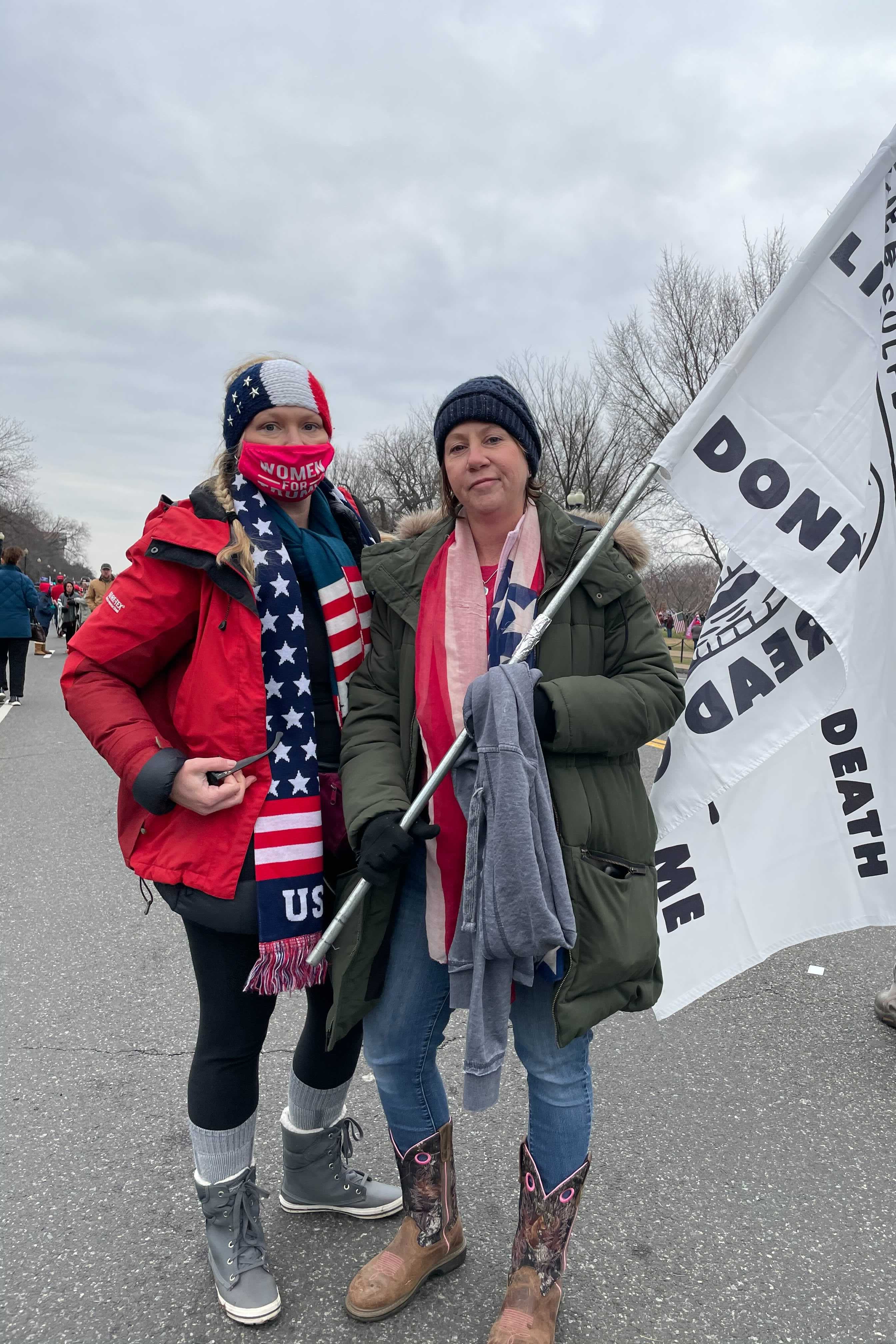 Two women, one masked, and one holding a Trump flag.